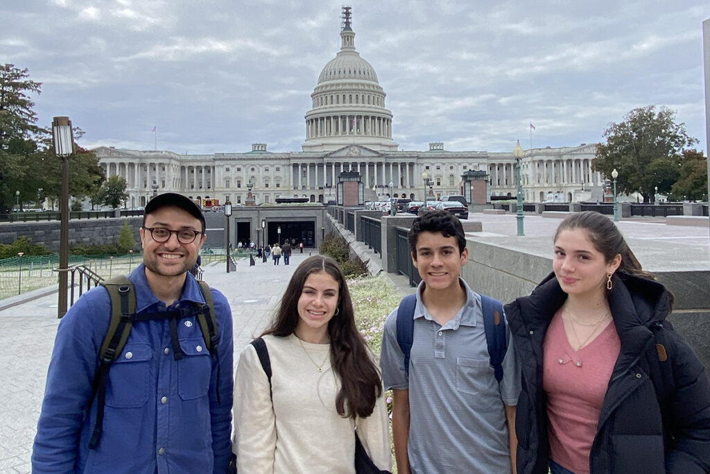 Students and a teacher pose in front of the United States Capitol building. 