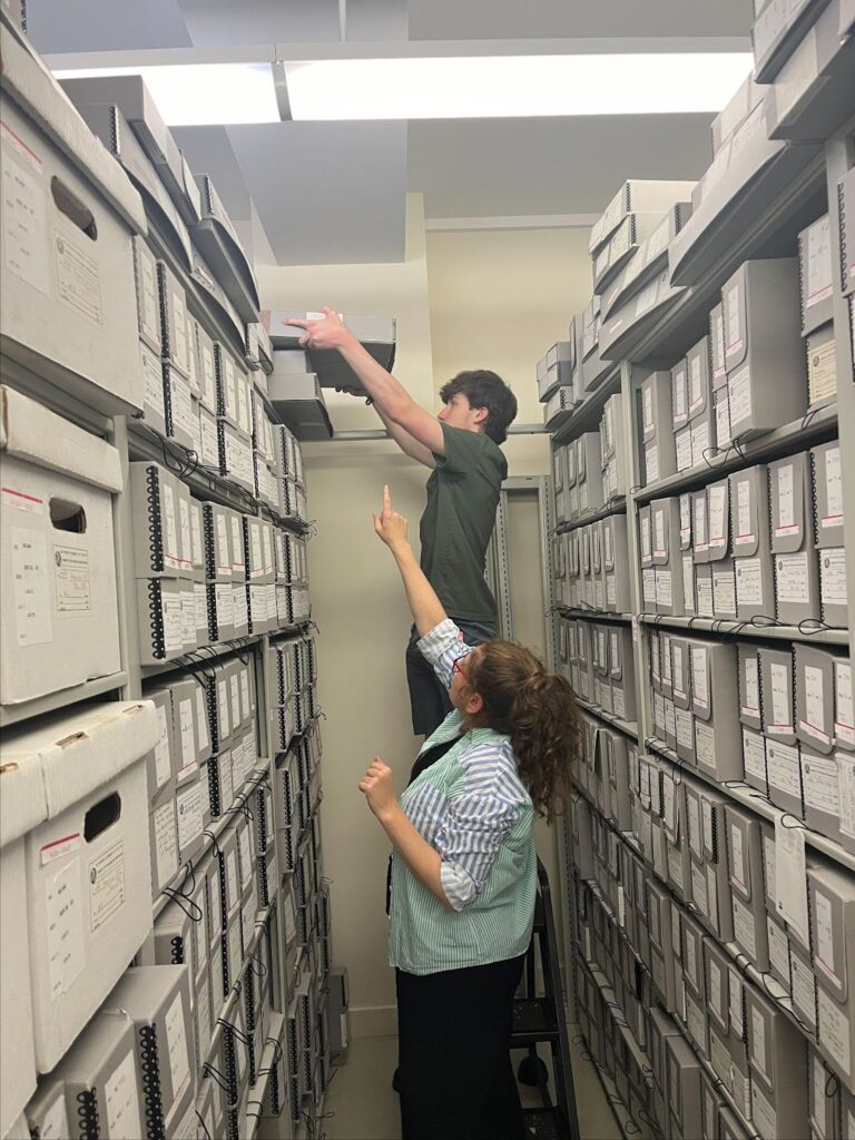 Two students reach for files in an archive room.